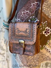 Load image into Gallery viewer, Brown hand tooled genuine leather saddle crossbody bag with floral tooling and vintage buckle detail worn on mannequin.