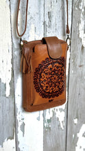 Load image into Gallery viewer, Front view of a handmade tan leather phone wallet crossbody with hand tooled Mandala design and tassel.