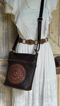 Load image into Gallery viewer, Chocolate brown mandala leather crossbody bag styled with a white bohemian dress, featuring turquoise accents and an adjustable shoulder strap.