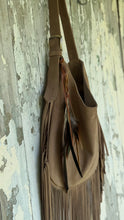 Load image into Gallery viewer, Side view of Wild Spirit suede leather fringe shoulder bag in taupe featuring feather detailing and a relaxed slouchy design.