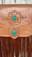 Load image into Gallery viewer, Close-up of intricate hand-tooled leather artwork and two turquoise stones on the Wild Sierra tan bohemian leather handbag.