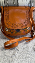 Load image into Gallery viewer, Boho tan leather crossbody bag featuring hand painted flowers, hand tooled detailing and an adjustable leather strap.